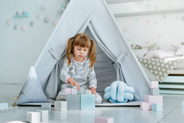 Mooi klein meisje met een pyjama spelend met houten speelgoed blokken in de kinderkamer. Selectieve focus. - Foto, afbeelding