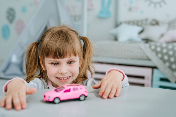Beautiful little girl wearing pajamas playing with pink toy car in the kids room. Selective focus. - Foto, Bild