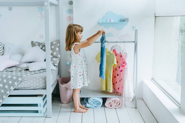 Beautiful little girl choosing a dress in the kids room. Selective focus. - Photo, image