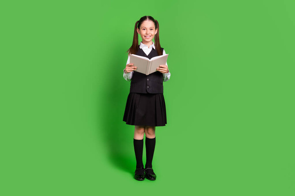 Full length body size view of attractive cheerful schoolgirl reading book isolated over bright green color background - Фото, зображення