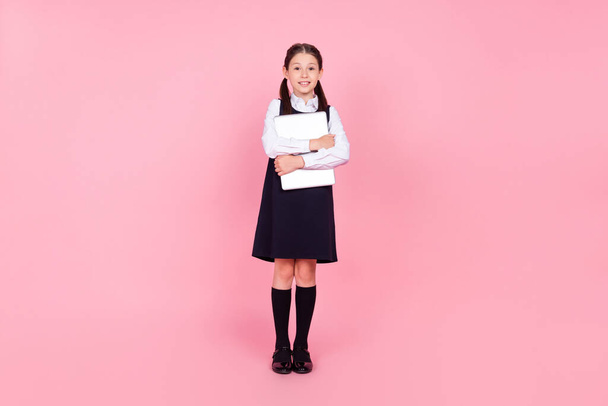 Full length body size photo schoolgirl in uniform embracing laptop smiling isolated pastel pink color background - Foto, Imagen