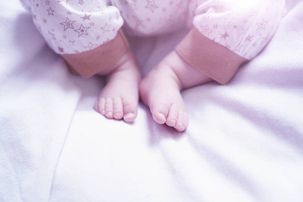 the babys legs are lying on a white bed - Фото, зображення