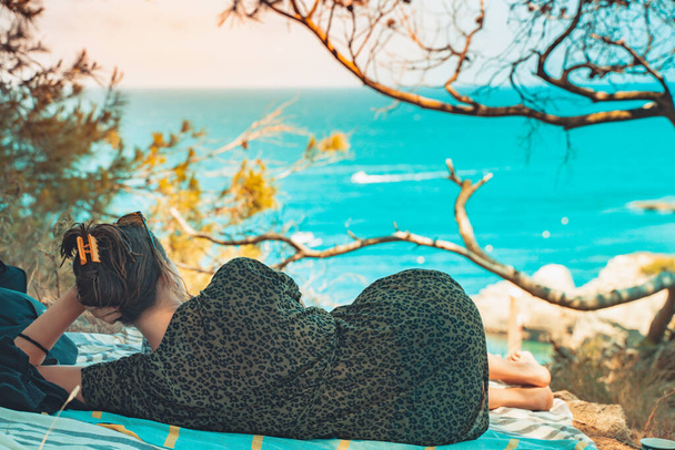 Beautiful woman standing and relaxing enjoy watching the sea view from the forest. Summer vibes. Adventure and travel female with leopard dress and sunglasses. Freedom, vacation and relax concept. - Фото, изображение