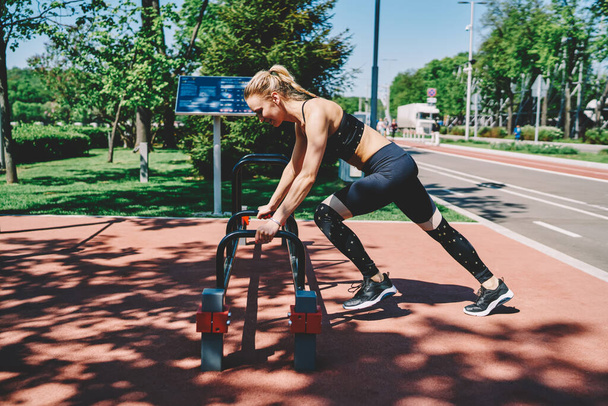 Side view of optimistic female in sportswear doing workout exercise leaning hands on horizontal bar at sport ground about track - Fotoğraf, Görsel