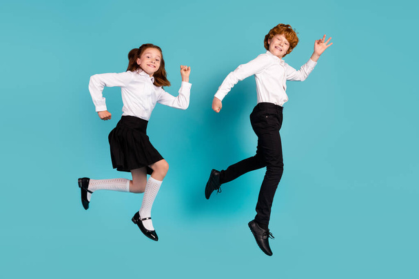 Full length body size view of two cheerful kids jumping walking good mood isolated over bright blue color background - 写真・画像
