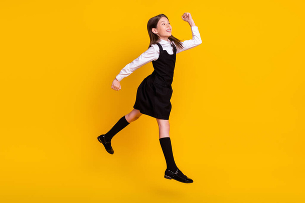 Full length body size side photo schoolgirl in uniform jumping gesturing like winner isolated vivid yellow color background - Фото, изображение
