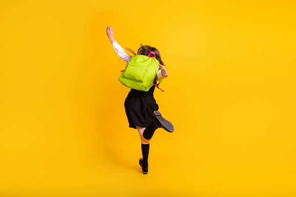 Фотография школьницы, идущей в школу с сумкой, изолированной ярким желтым цветом на фоне - Фото, изображение