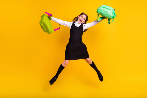 Full length body size photo schoolgirl jumping two rucksacks angry furious isolated bright yellow color background - Fotografie, Obrázek
