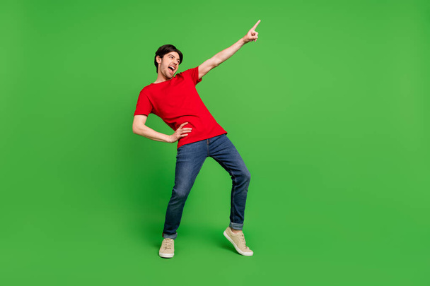 Photo of excited crazy guy dance direct finger empty space wear red t-shirt isolated green color background - Fotó, kép