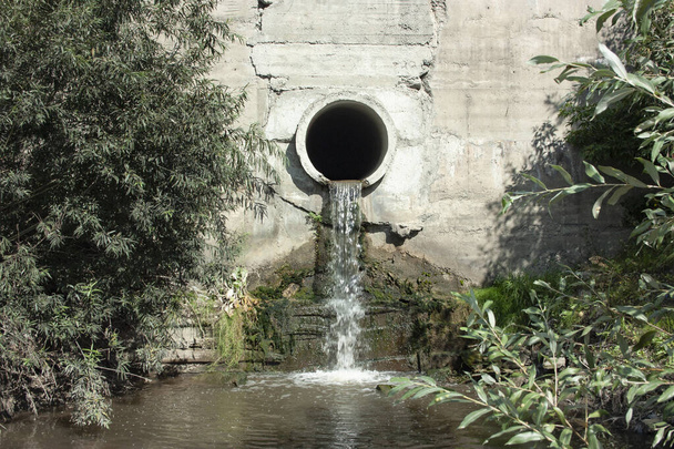 Aguas residuales o aguas residuales fluyen fuera de la tubería de drenaje hacia el río - Foto, Imagen