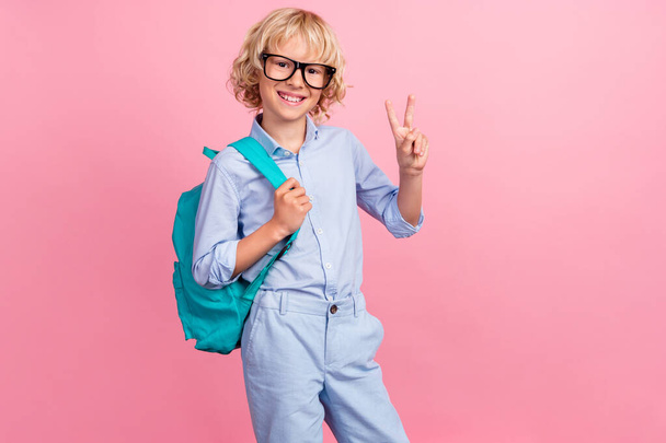 Photo of funky cool school boy wear blue shirt glasses backpack smiling showing v-sign isolated pink color background - Foto, Imagem