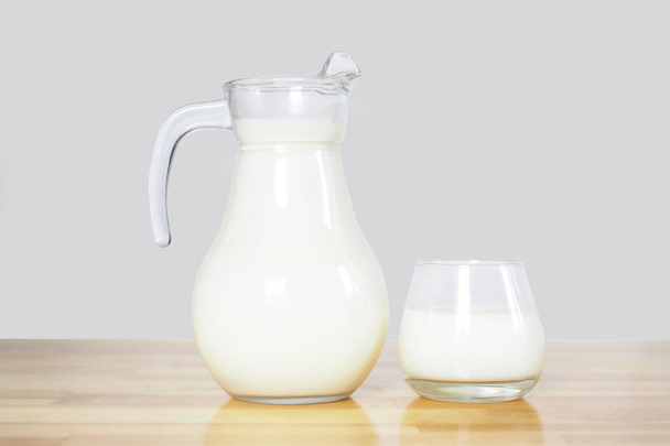 milk in a glass and a jug on a wooden table on a gray background. copy space - Foto, imagen