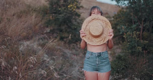 Portrait de femme gaie avec chapeau de paille regardant la caméra avec une émotion heureuse et des grimaces en plein air au coucher du soleil - Séquence, vidéo