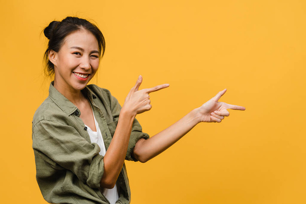 Portret van jonge Aziatische dame glimlachend met vrolijke uitdrukking, toont iets verbazingwekkends op lege ruimte in casual doek en kijkend naar camera geïsoleerd over gele achtergrond. Gezichtsuitdrukking. - Foto, afbeelding
