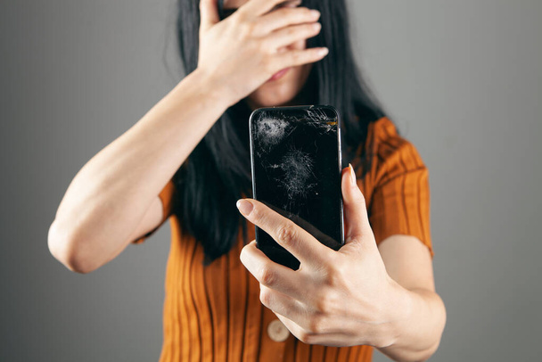 женщина показывает сломанный экран телефона на сером фоне - Фото, изображение