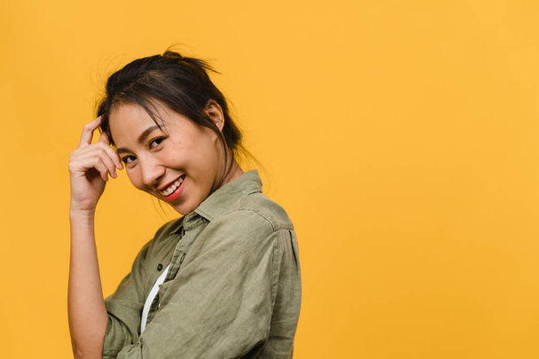 Fiatal ázsiai hölgy pozitív arckifejezéssel, széles mosollyal, alkalmi ruhába öltözve, és a kamerát sárga háttérrel. Boldog imádnivaló boldog nő örül a sikernek. Az arckifejezés fogalma. - Fotó, kép