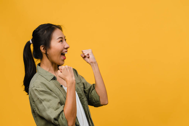 Young Asia lady with positive expression, joyful and exciting, dressed in casual cloth over yellow background with empty space. Happy adorable glad woman rejoices success. Facial expression concept. - Photo, Image