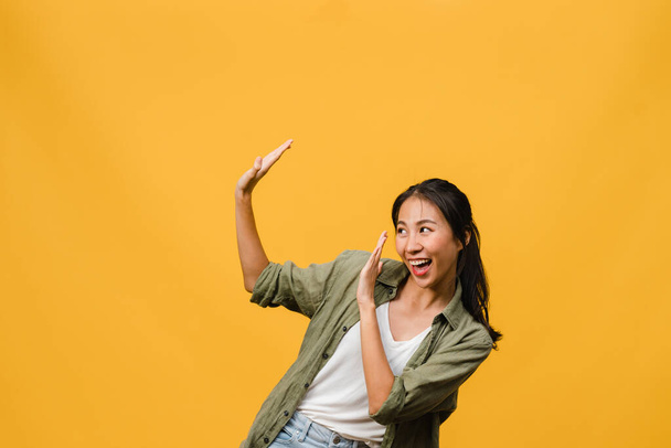 Portrét mladé asijské dámy s pozitivním výrazem, široce se usmívající, oblečené v neformálním oblečení přes žluté pozadí. Šťastná rozkošná šťastná žena se raduje z úspěchu. Koncept výrazu obličeje. - Fotografie, Obrázek