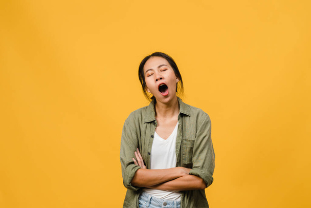 Retrato de una joven asiática con expresión negativa, aburrida bostezando cansada cubriendo la boca con la mano en ropa casual aislada sobre fondo amarillo con espacio para copiar en blanco. Concepto de expresión facial - Foto, imagen