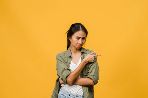 Young Asia Lady shows something amazing at blank space with negative expression, excited screaming, crying emotional angry looking at camera isolated over yellow background. Facial expression concept. - Fotoğraf, Görsel