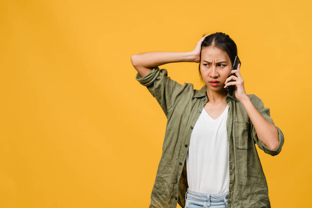 Young Asia lady talk by phone with negative expression, excited screaming, cry emotional angry in casual cloth and stand isolated on yellow background with blank copy space. Facial expression concept. - Φωτογραφία, εικόνα