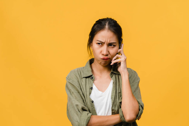 Fiatal ázsiai hölgy beszélni telefonon negatív arckifejezéssel, izgatott sikoltozás, sírni érzelmi dühös alkalmi ruhát, és állni elszigetelt sárga háttérrel üres másolás helyet. Az arckifejezés fogalma. - Fotó, kép