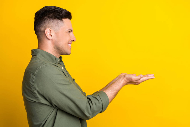 Side profile photo portrait man smiling keeping copyspace on hands isolated vivid yellow color background - 写真・画像