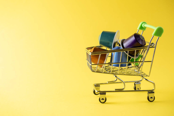 A food basket full of colorful aluminum coffee capsules on a yellow background. Side view, copy space - Photo, Image