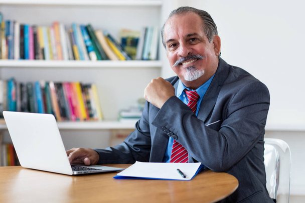Hispanic senior adult businessman at computer at desk at office - Fotó, kép