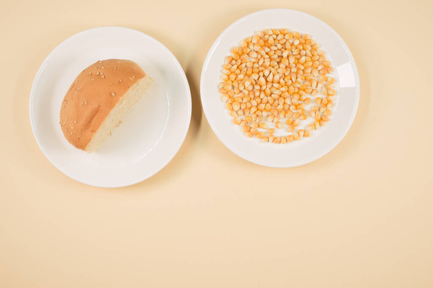A top view of half bread bun and corn grains on a plate isolated on light orange background - Fotoğraf, Görsel