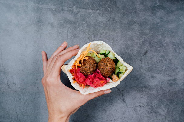 A top view shot of a hand holding a vegetarian falafel with vegetables wrapped in pita bread - 写真・画像