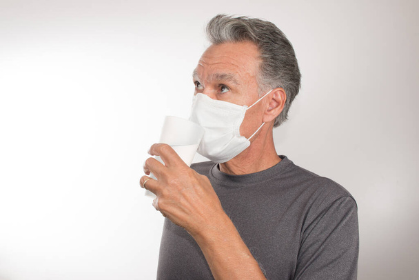 Senior Man trying to Drink Water while still wearing his Surgical Mask - Photo, Image