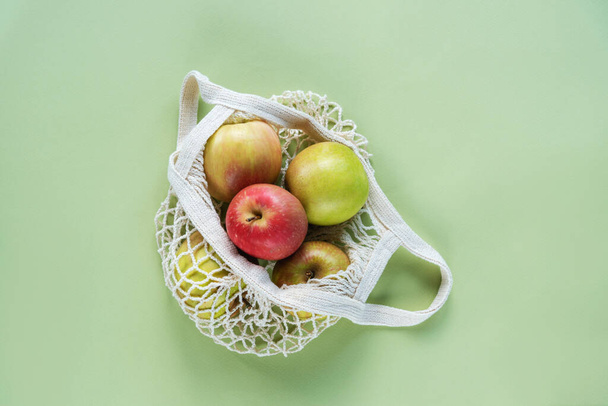 Manzanas frescas maduras en una bolsa de hilo sobre fondo verde. Cero residuos, sin concepto plástico. Vista superior, plano. - Foto, imagen