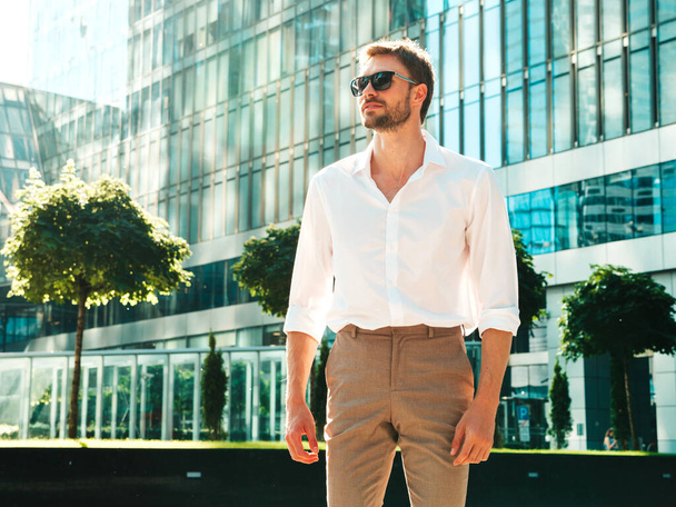 Portrait of handsome confident stylish hipster lambersexual model.Modern man dressed in white shirt. Fashion male posing in the street background near skyscrapers in sunglasses - Fotoğraf, Görsel