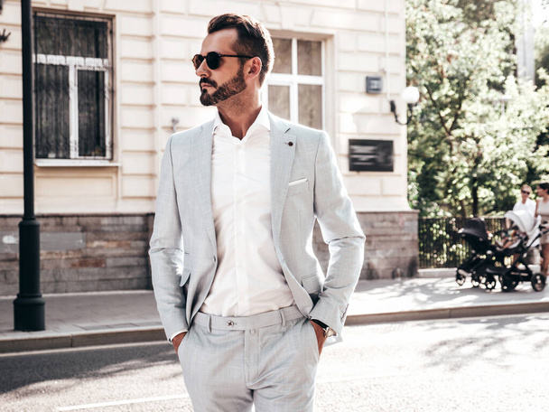 Portrait of handsome confident stylish hipster lambersexual model.Modern man dressed in elegant white suit. Fashion male posing in the street background in Europe city at sunset. In sunglasses - Foto, Imagem