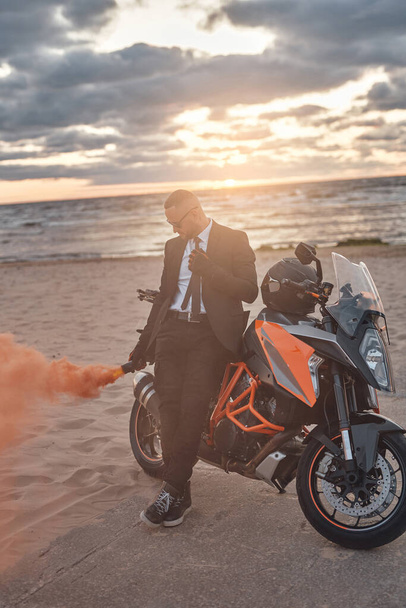 Elegante hombre con bomba de humo y moto en la playa - Foto, Imagen