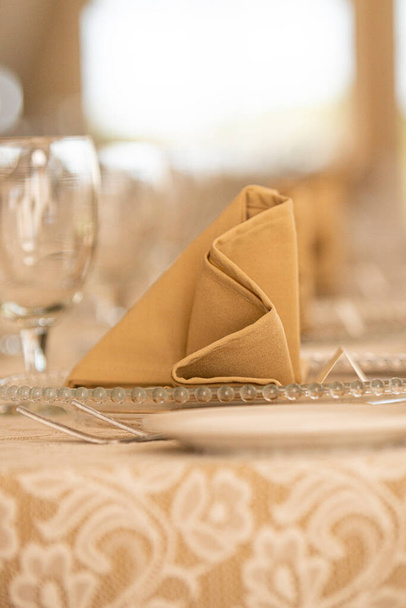 Filas de servilletas plegadas de lino beige en platos de vidrio durante la cena - Foto, imagen