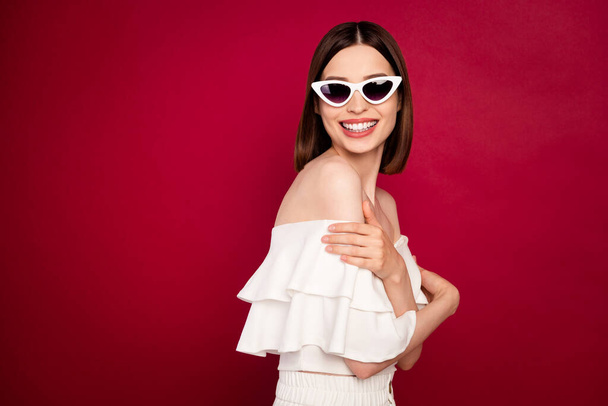 Profile photo of cute brown hairdo young lady hug herself wear eyewear white bare shoulders blouse isolated on red background - Fotó, kép