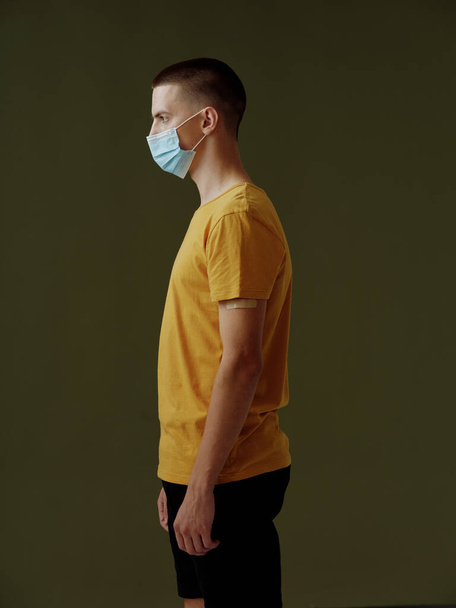 mies keltaisessa t-paidassa tummalla taustalla lääketieteellinen naamio puolella näkymä - Valokuva, kuva