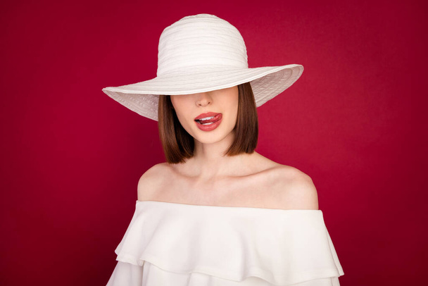 Photo portrait jolie brune portant un chapeau couvrant les yeux léchant les lèvres isolé fond de couleur rouge - Photo, image
