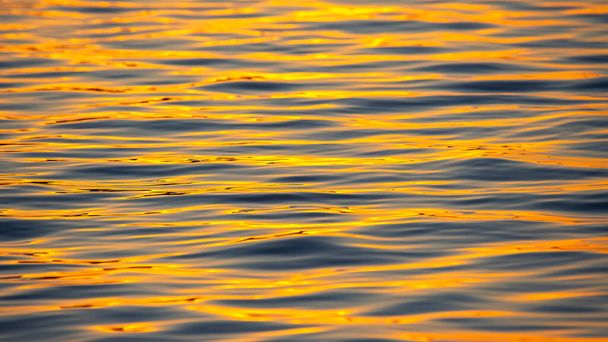 Odbicie zachodzącego słońca w fali wody. Naturalna tekstura tła - Zdjęcie, obraz