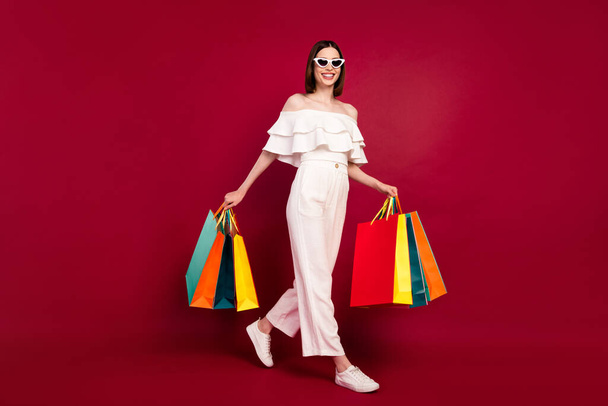 Full length body size photo pretty brunette keeping bags in shopping mall isolated red color background - Фото, изображение