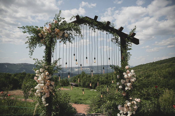 Wedding arch on boho style with white flowers in park with light bulbs. - Zdjęcie, obraz