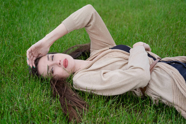 魅力的なブルネットは緑の芝生に横たわっています。疲れててマジで. - 写真・画像