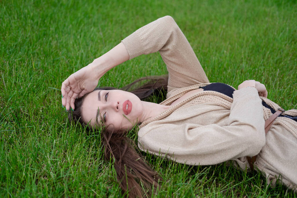 charming brunette lies on green grass. Tired, serious. - Zdjęcie, obraz
