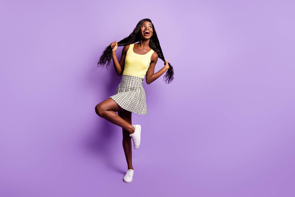 Full size photo of optimistic curly lady stand look empty space wear green top skirt sneakers isolated on vibrant purple background - Photo, Image