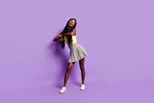 Full size photo of optimistic curly lady dance look empty space wear green top skirt sneakers isolated on vibrant purple background - Fotoğraf, Görsel