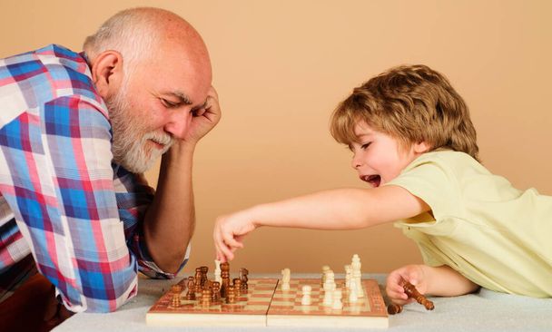 Ευτυχισμένο μικρό παιδί που παίζει σκάκι με τον παππού. Οικογενειακή σχέση με τον παππού και τον εγγονό. Παππούς και εγγονός παίζουν επιτραπέζιο παιχνίδι. - Φωτογραφία, εικόνα