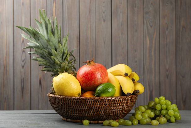 Wicker bowl with different ripe fruits on wooden table - Φωτογραφία, εικόνα