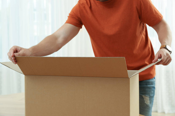 Man opening parcel indoors, closeup. Internet shopping - Foto, afbeelding